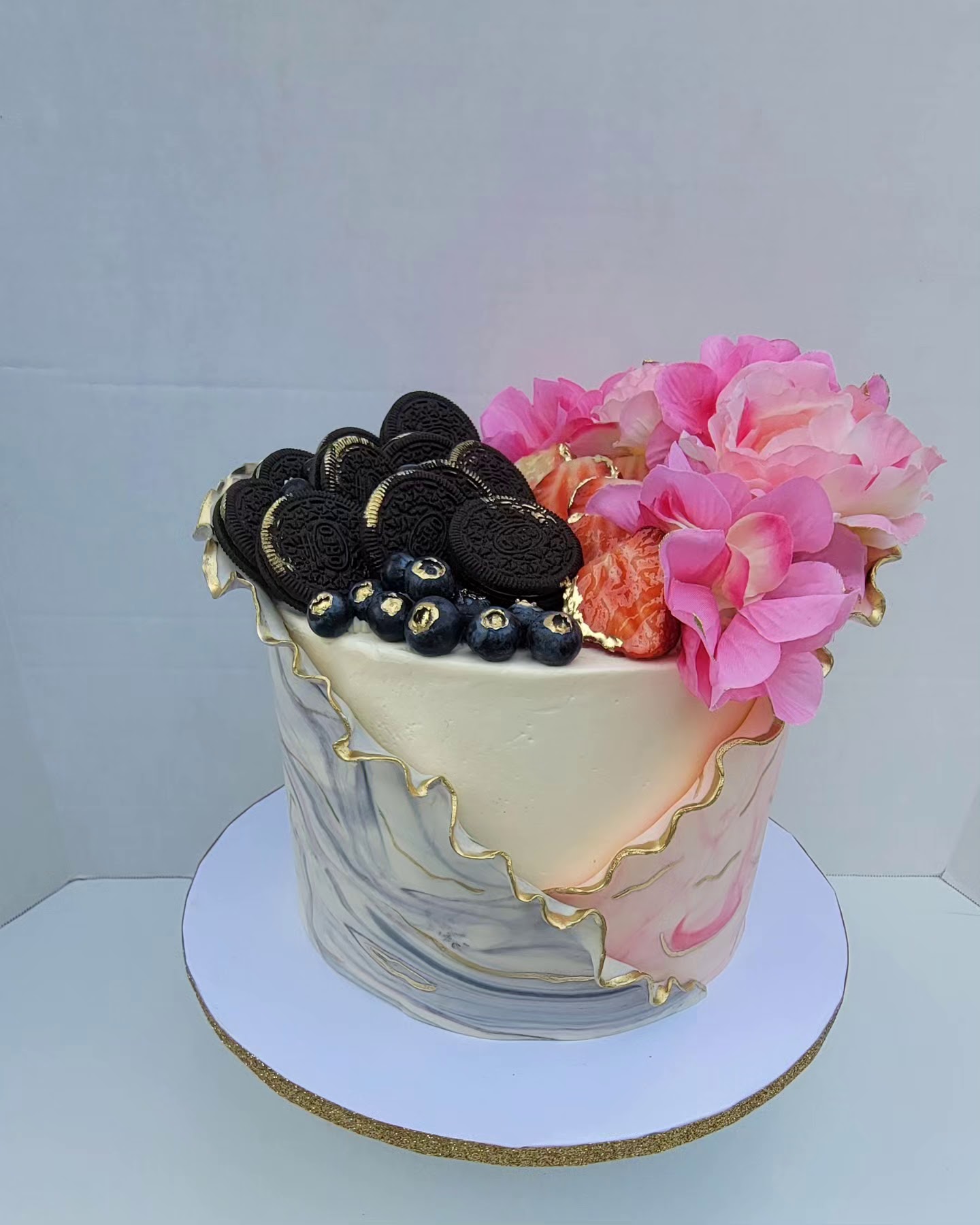 Gâteau cylindrique crème avec wrap marbré gris et rose bordé d'or, Oreos, fraises, bleuets et pivoines.